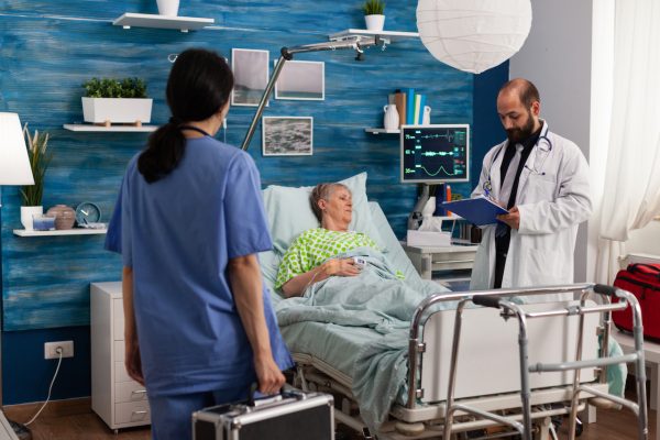 Caregiver nurse man writing medication treatment on clipboard discussing healthcare assistance. Senior woman resting in bed during Social services nursing elderly retired female. Support assistance