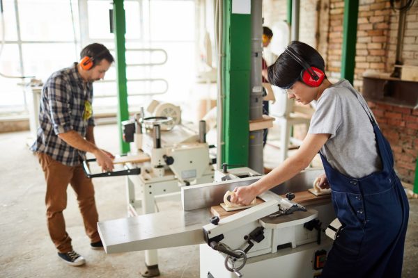 Side view portrait of carpenters using machines in joinery workshop, copy space